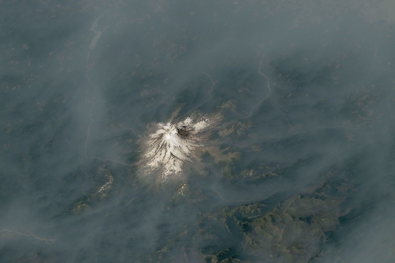 Photograph taken from the International Space Station looking obliquely across a smoke layer, with a snow-capped Cascade volcano rising through it