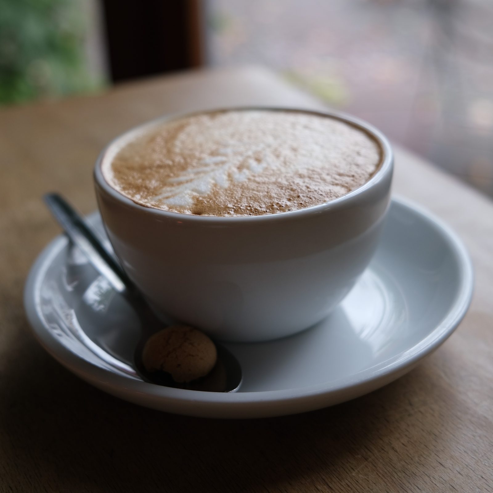 A cup of coffee with a thick crema, on a saucer with a spoon, on a wooden table