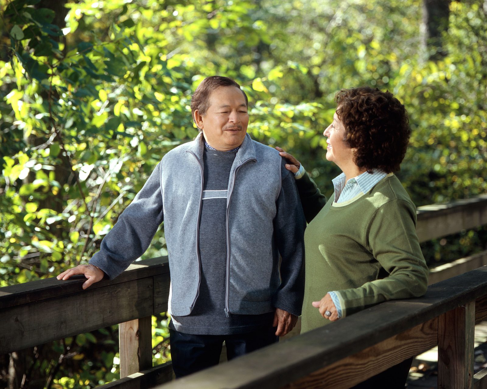 Two adults in late middle age standing outdoors by a wooden rail, talking
