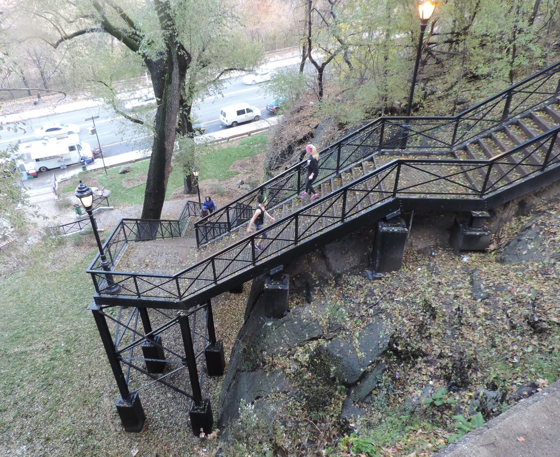 Two people in athletic wear climbing an outdoor metal staircase in a park