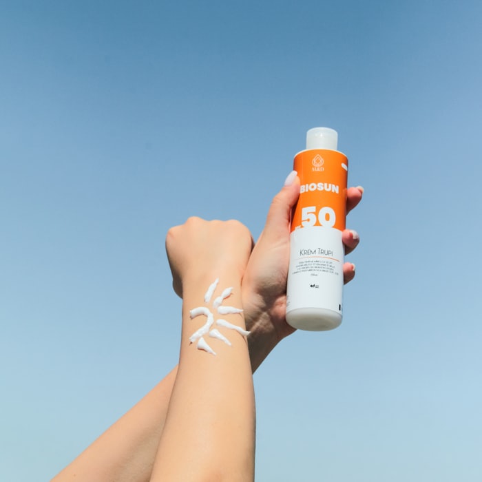 Hand holding a sunscreen bottle, sunscreen streaked across the forearm