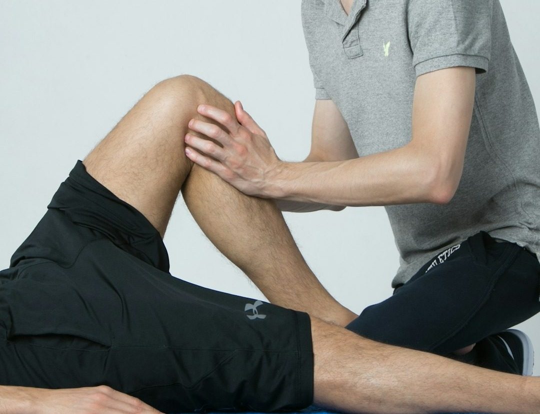 A clinician's hands mobilising a patient's knee, cropped close so neither face is visible