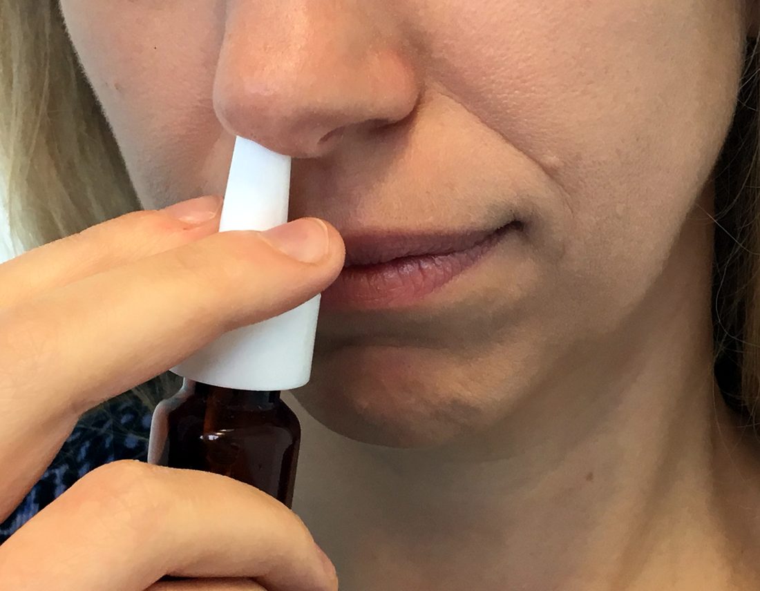 A person holding a small brown glass bottle to one nostril and pressing the white pump