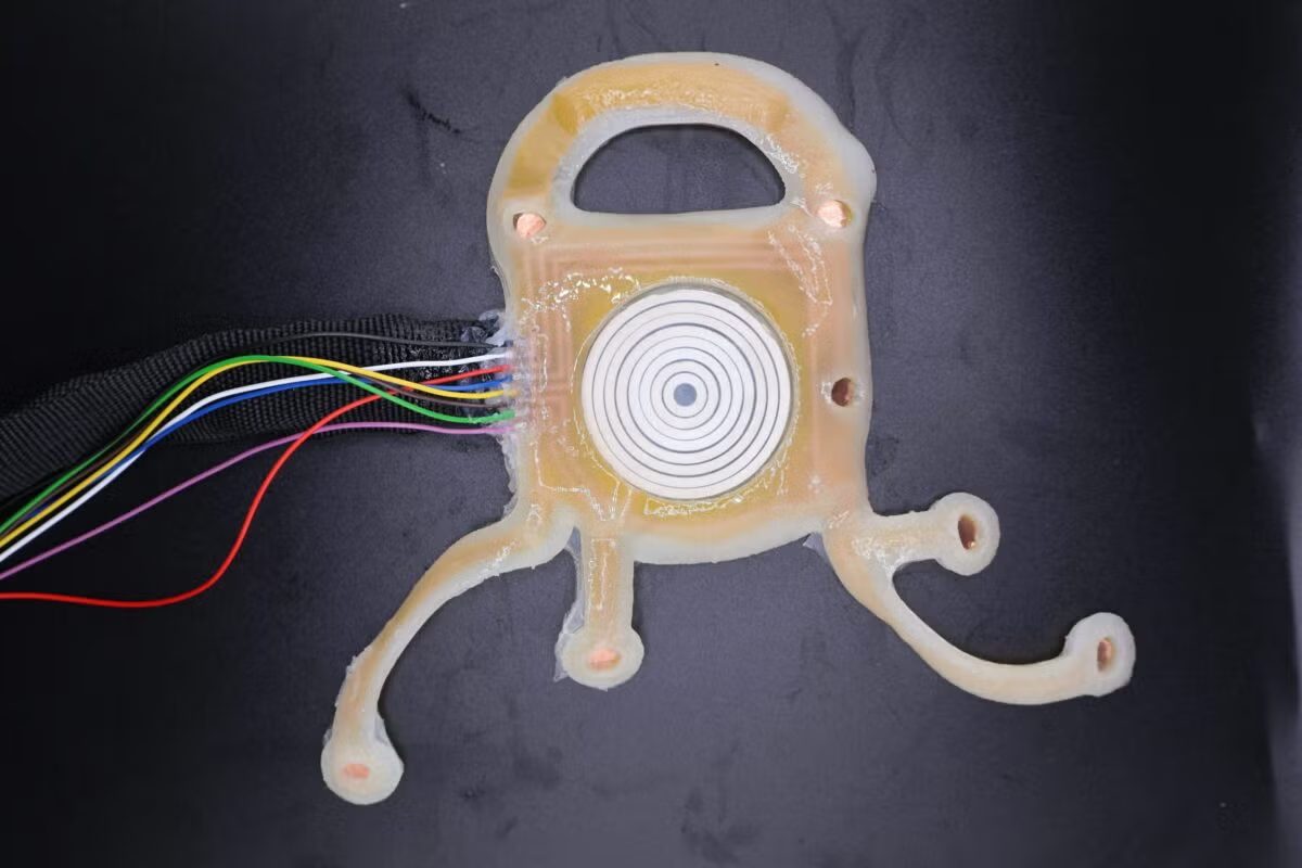 The soft skin patch used in the UT Austin sleep study: a pale flexible device with a circular ultrasound transducer at its centre and a ribbon of coloured wires leaving one edge