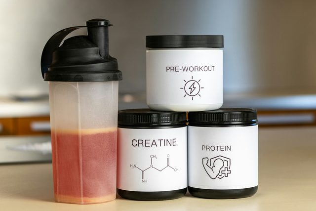 Three tubs of protein powder standing next to a blender on a kitchen counter