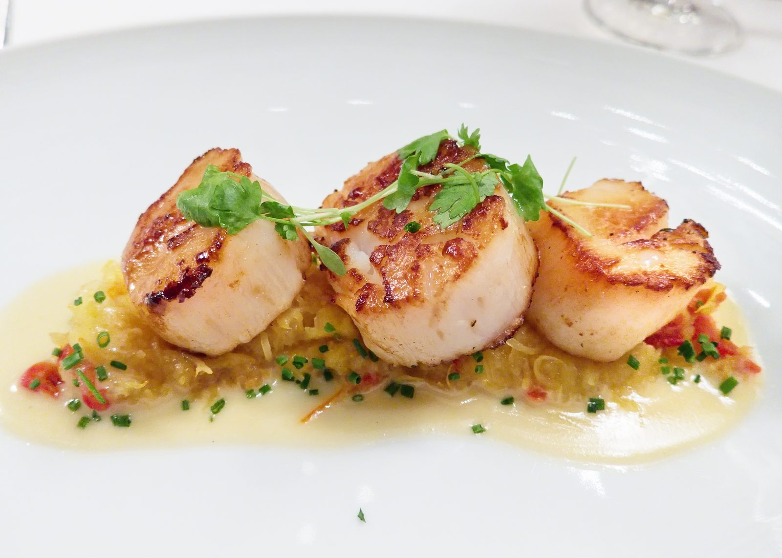 Three golden seared scallops plated over a bed of spaghetti squash and tomato confit, finished with chives and a light butter sauce