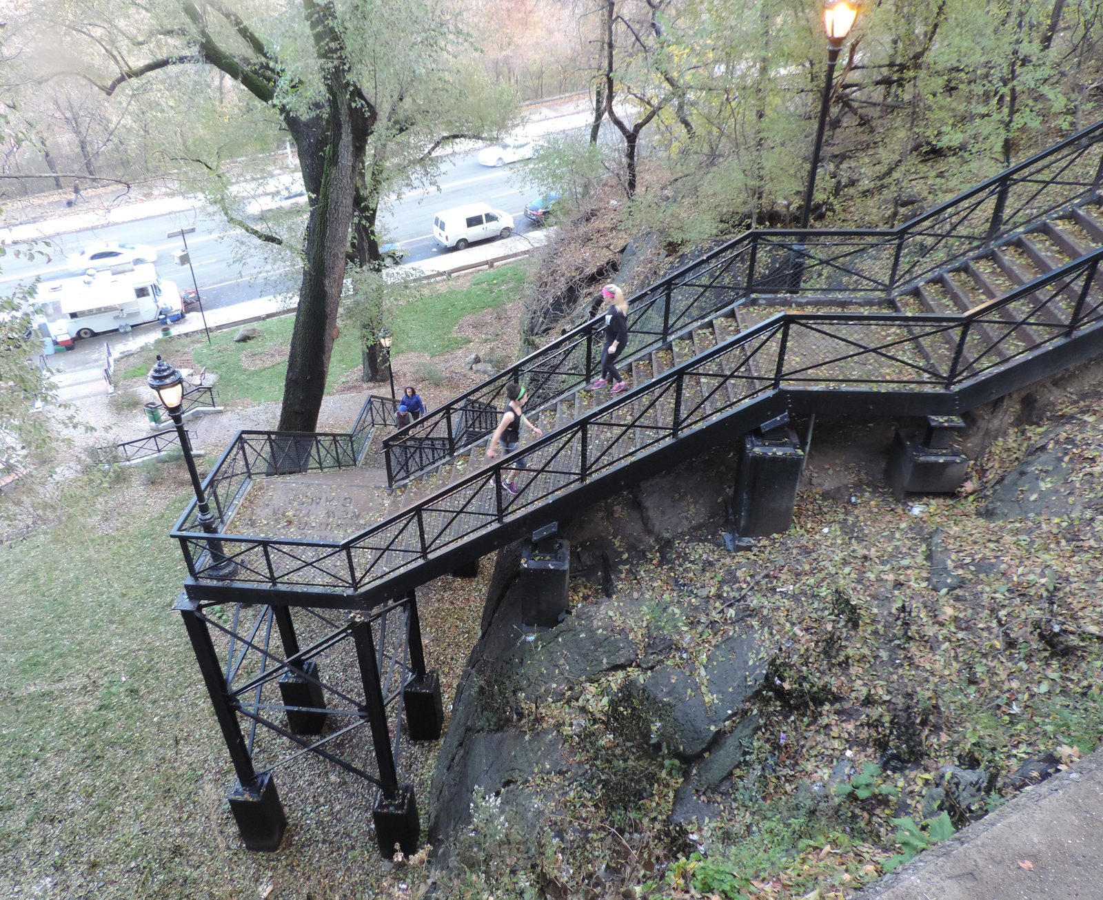 Two people in athletic wear climbing an outdoor metal staircase in a park
